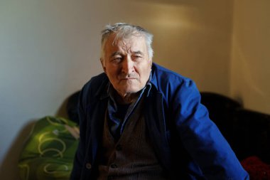 Yaşlı, beyaz, yaşlı bir adam huzurevinde tek başına oturuyor. Belden yukarı, beyaz saçlı, yalnız bir erkek. Balkan çiftçisinin düşünceli bakışları.