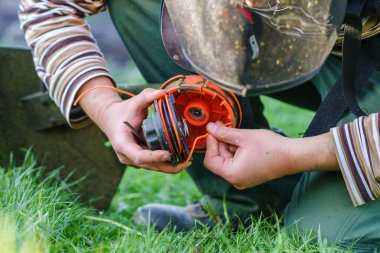 Close up on string trimmer head unknown caucasian man holding and repairing weed cutter replacing parts replacement in day on the field farmer or gardener clipart
