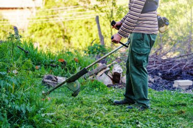Tanınmayan Kafkasyalı erkek çiftçi bahçıvanın orta kesiminde çim biçme makinesi ile çim biçmeye hazır, güneşli bir günde tarlada ot kesmeye hazır.