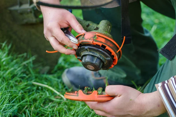 Close up on string trimmer head unknown caucasian man holding and repairing weed cutter replacing parts replacement in day on the field farmer or gardener