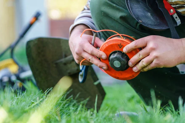 Close up on string trimmer head unknown caucasian man holding and repairing weed cutter replacing parts replacement in day on the field farmer or gardener