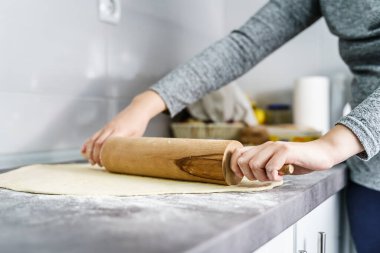 Evdeki mutfak tezgahında merdane kullanarak kruvasana hamur ezmesi hazırlayan kimliği belirsiz beyaz kadının ellerini kapatın. Ev yemekleri ve fırın konsepti.