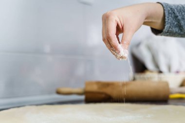 Elinde un tutan ve mutfak tezgahına hamur serpiştiren ev yapımı macun veya kruvasan yapan kimliği belirsiz bir kadını yakından takip edin.