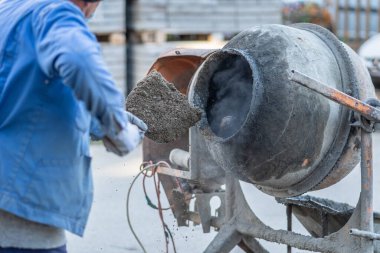 İnşaat alanındaki mikserde beton harç karışımı yapmak için kürek kullanan bilinmeyen bir adam miksere özel olarak odaklanmış.