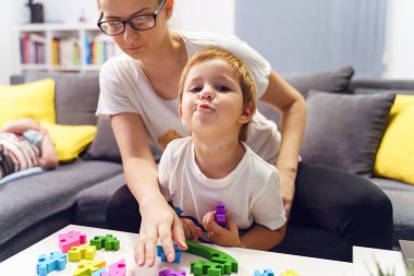 Evdeki kanepede annesiyle oyun oynarken kameraya bakan küçük beyaz bir çocuğun ön manzara portresi. Aile bağlarını kuvvetlendirme konsepti.