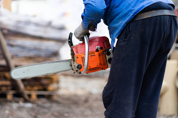 Средняя часть человека держит бензопилу осенью или зимой во дворе на открытом воздухе