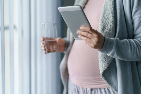 未知の原因不明の女性の手に閉じるU妊娠中の母親が窓のそばに立っている間 水とデジタルタブレットのガラスを保持 妊娠と飲料水の概念 — ストック写真