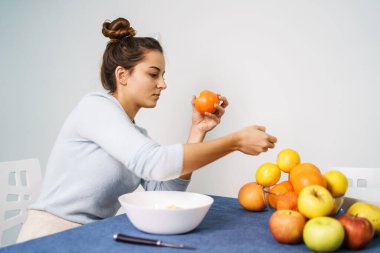 Genç bir kadının portakal soyarken evde oturup sağlıklı bir şekilde organik vejetaryen yemekleri yemesini izlemek.