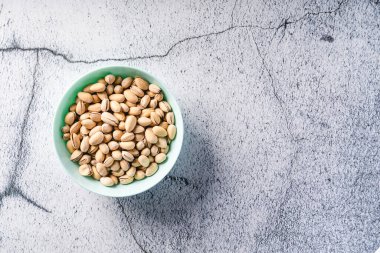 Taze kavrulmuş şam fıstıklarının üst görüntüsü. Fıstıklar kasede. Beton masa zemininde de fotokopi alanı var.