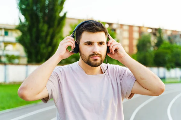 Male jogger adjusting earphones while training outdoor in summer day - recreation and healthy lifestyle concept