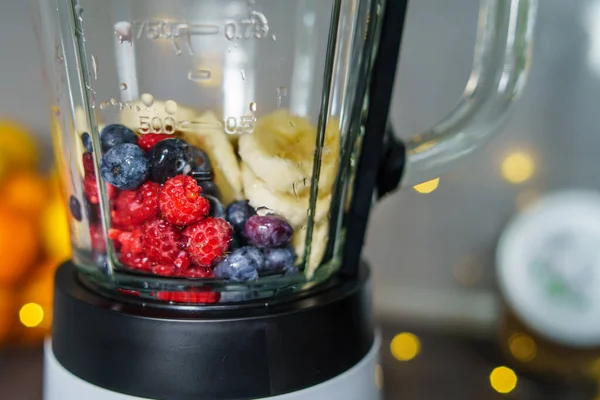 front view on fruits in blender - fresh organic blueberries raspberries and bananas in blender ready for making smoothie - healthy eating vegan concept