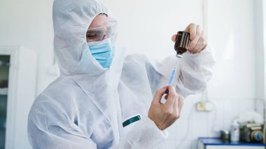Kafkas erkek sıhhiye doktorunun, Corona-virüsü aşılama ve aşı konsepti için klinikte şırınga ve iğne enjekte etme dozunu hazırlarken yan görüntüsü.
