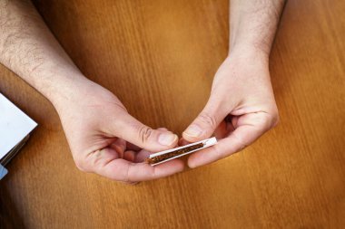 Kahverengi ahşap masa üzerinde sigara tütünü saran, kimliği belirsiz beyaz adamın ellerine yakın çekim yapın.