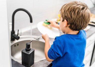 Bilinmeyen beyaz erkek ya da kızın mutfak lavabosunun yanında durup bulaşık yıkaması - çocuk ev işlerine yardım ederken - büyüyen bağımsızlık kavramı kopyalama alanı