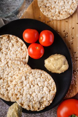 Sehpada gevrek pirinç kekleri ve domates sebzeleri ve masada susam tohumları. Sağlıklı vejetaryen ya da vejetaryen kahvaltısı glütensiz.