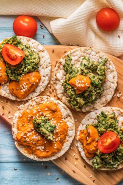 Masada gevrek pirinç kekleri ve humus yayılmış ıspanaklı yumurta, domates ve sebzeli ıspanak. Sağlıklı vejetaryen kahvaltısının glütensiz üst görüntüsü.