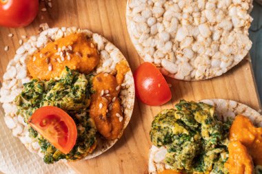 Masada gevrek pirinç kekleri ve humus yayılmış ıspanaklı yumurta, domates ve sebzeli ıspanak. Sağlıklı vejetaryen kahvaltısının glütensiz üst görüntüsü.