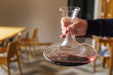 Close up on hand of unknown caucasian man holding decanter with red wine in the hall at home or restaurant with copy space clipart