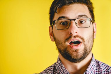 Gözlüklü, sarı arka plandaki kameraya bakan hayret verici adam. Kopya alanını kapat.