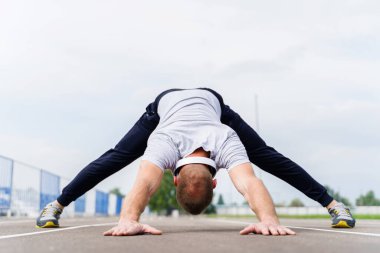 Yetişkin beyaz bir adamın koşu pistinde esnemesine düşük açılı bakış açısı - sarışın erkek sporcu güneşli bahar ya da yaz gününde antrenmana hazırlanıyor - gerçek insanlar sağlıklı yaşam tarzı konsepti