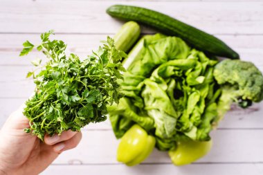 Masanın üzerinde yeşil maydanozu çeşitli sebzelerle tutan Kafkasyalı adamı yakından takip edin. Parlak filtre çiğ vegan ve vejetaryen gıda sağlıklı beslenme kavramı.