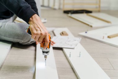 Bilinmeyen bir beyaz adamın elinde elektrikli tornavida tutarken, direktifler doğrultusunda kontrplak vidalarının mobilyalarını monte ederken, orta kısmına yaklaş - DIY konsepti kopyalama alanı