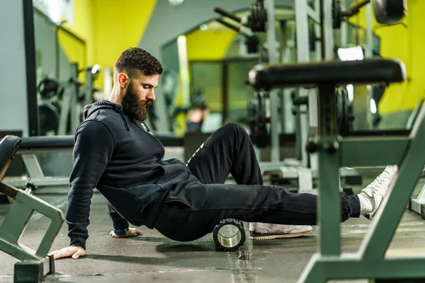 stock image Sport man Using black Foam Roller for Muscle and Fascia Stretching leg - Male athlete relieve sore muscles after a training workout at gym - health and fitness sport body care concept