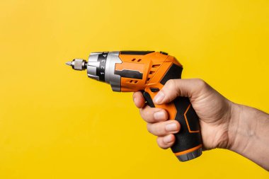 Elinde elektrikli tornavida tutan bilinmeyen bir adamın eli. Parlak sarı arka planda çalışan bir erkek el işi. Yenileme elektrikli ekipmanları tamir ediyor.