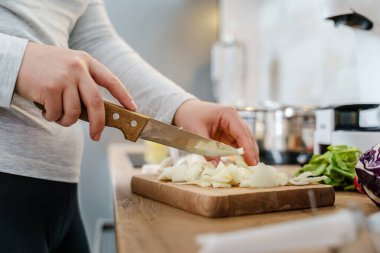 Mutfakta bıçaklı, vejetaryen ya da vejetaryen çorbası için soğan doğrayan organik sebzelerden sağlıklı yemek pişiren kimliği belirsiz bir kadının ellerinde.