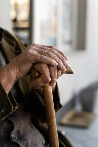 Close up on hands of unknown old caucasian man pensioner senior holding cane walking stick while sitting and waiting - real people old age senility concept copy space