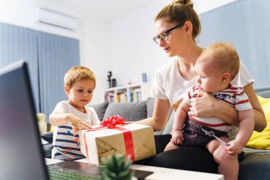 Anne ve iki oğlu oğluna hediye kutuları verirken evde kanepede oturup doğum gününü kutluyor ya da çocuklar için hediyelerle baş başa tatil yapıyor.