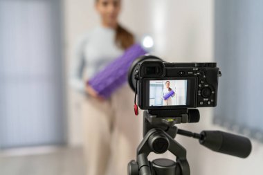 Online eğitim için kamera önünde genç beyaz bir kadının videosunu kaydetmek ve yayınlamak - odada spor yapmak için köpük silindiri kullanan kız - sağlık ve fitness konsepti