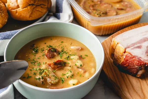 Böbrek fasulyesi çorbası füme sosis ve domuz pastırması masada.