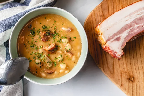 Böbrek fasulyesi çorbası füme sosis ve domuz pastırması masada.