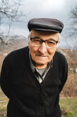 Baharda ya da sonbaharda ayakta duran yaşlı beyaz adamın portresi. Çiftliğin kırsalında dikilip kameraya bakan neşeli erkek çiftçinin portresi. Gerçek insanlar kavramı.