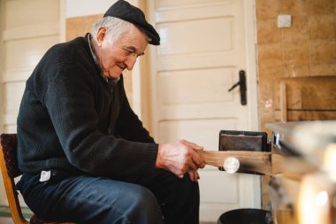 Yaşlı, beyaz, büyükbaba çiftçi, çiftlikteki ocağının yanında oturmuş şöminenin üzerine odun koyuyordu.