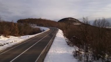Kış günü Sırbistan 'ın Knjazevac kenti yakınlarında beyaz karla kaplı dağ sırasındaki ağaçlar ve ormanlar boyunca kıvrımlı yılanlı yolda yükselen hava aracı videosu - Seyahat yolculuğu konsepti