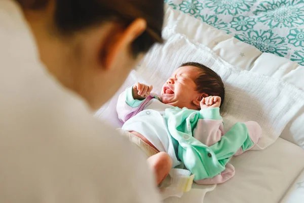 Unknown woman mother taking care of her baby boy or girl putting on clothes - newborn caucasian infant cry on bed having cramps while mom change diapers on bed at home - nursing motherhood concept