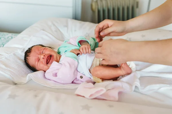 Unknown woman mother taking care of her baby boy or girl putting on clothes - newborn caucasian infant cry on bed having cramps while mom change diapers on bed at home - nursing motherhood concept