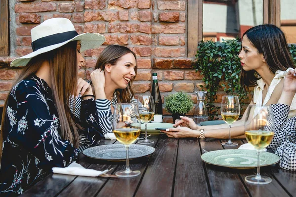 Group of caucasian women female friends sitting at the table at restaurant having a discussion or argument with different reaction smiling and accusing being angry about mobile phone messages cheating