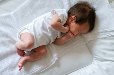 Yeni doğmuş iki haftalık beyaz bir bebek evde yatakta uyuyor. Sevimli küçük bir kız çocuğu huzur içinde uyur.