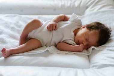 Yeni doğmuş iki haftalık beyaz bir bebek evde yatakta uyuyor. Sevimli küçük bir kız çocuğu huzur içinde uyuyor.