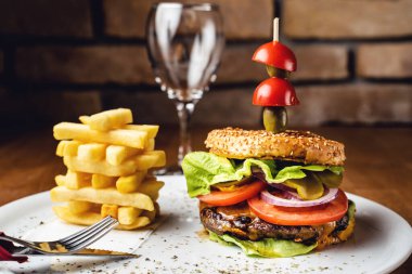Sığır etli soğanlı burger ve duvar arkası tuğlalı bir tabakta marul yaprakları restoranda patates cipsi servis edilen burger.