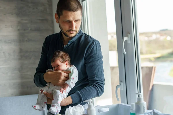 Caucasian man male father standing by the window at home holding his newborn baby daughter or son in day father\'s day parenthood real people concept