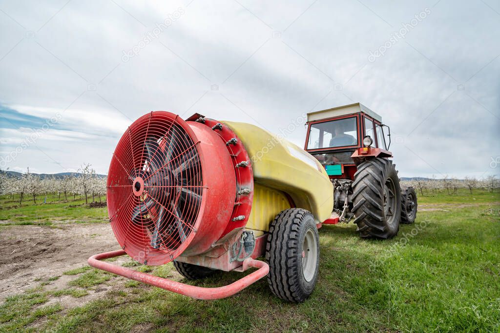 Tractor with agricultural sprayer machine with large fan ready to spray insecticide or pesticide in orchard agriculture concept back view