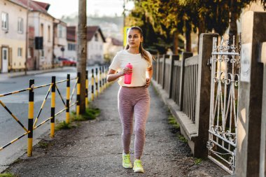 Güneşli bir günde şehrin kaldırımlarında koşan, spor antrenmanı ve eğlence konsepti olan beyaz kadın ön cephede.