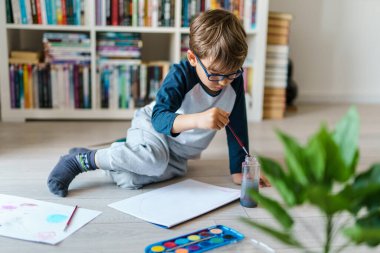 Evinde yerde oynayan dört yaşındaki beyaz çocuk hakkında ön görüş - suluboya resim yaparken boya kullanan küçük bir çocuk sanatsal beceriler geliştiriyor, boş zamanlarını ve yaratıcı eğitimi geliştiriyor.