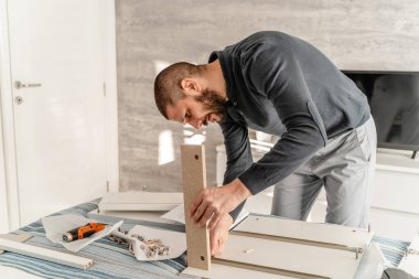 Tek başına sakallı bir adam elinde elektrikli tornavidayla evde mobilya topluyor ve parçaları birleştiriyor - yarım boy ön görüş konsepti gerçek insanlar boşluğu kopyalıyor