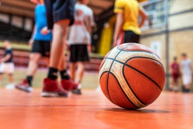 Spor salonunda yerde basketbol topu. Sahada seçici bir odak. Antrenman sporu ve gelişim konseptinde bilinmeyen çocukların ayakları bulanık.