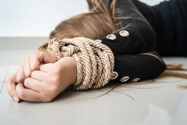 Close up on hands of Unknown caucasian woman or minor girl lying unconsciousness on the floor with rope tied arms - Human rights kidnapping trafficking violence concept selective focus clipart